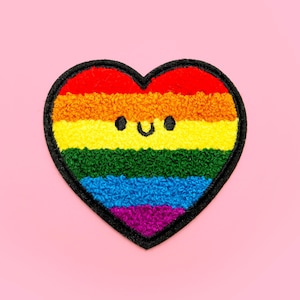 May include: A rainbow heart-shaped patch with a smiling face. The patch is made of fuzzy fabric and has a black outline.