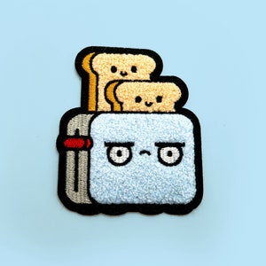 May include: A blue embroidered patch of a toaster with a grumpy expression and two slices of bread popping up. The toaster has a red lever and a black outline.