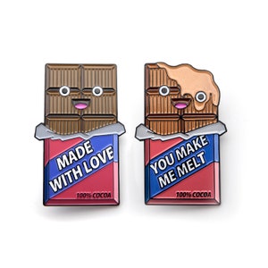 May include: Two enamel pins shaped like chocolate bars with cartoon faces. The left pin says "Made with Love" and the right pin says "You Make Me Melt". Both pins have the text "100% Cocoa" at the bottom.