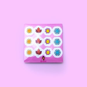 Op de afbeelding: Een vel stickers met een roze achtergrond met negen verschillende ontwerpen. De ontwerpen omvatten een zon, een blad, een bloem en een sneeuwvlok. Elk ontwerp wordt drie keer herhaald.