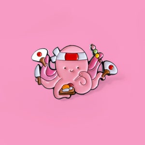 Op de afbeelding: Een roze octopus met een rood hoofdband die een sushi-plateau, eetstokjes en een mes vasthoudt. De octopus is een metalen pin.