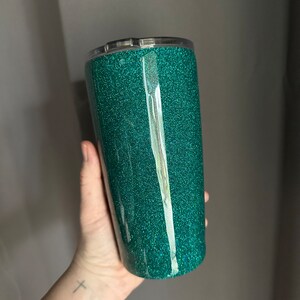 May include: A teal green tumbler with a glitter finish. The tumbler has a clear lid and is made of stainless steel.
