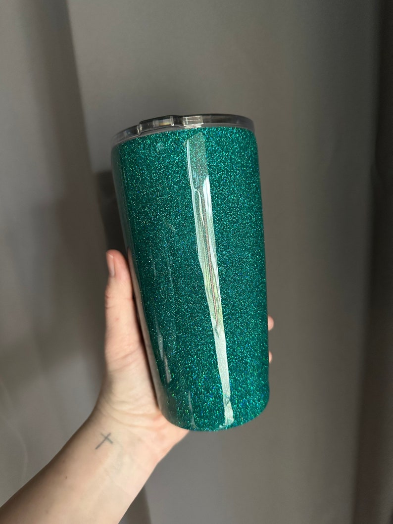 May include: A teal green tumbler with a glitter finish. The tumbler has a clear lid and is made of stainless steel.