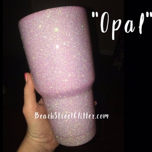 May include: A pink glitter tumbler with the text "Opal" on the side. The tumbler is made of stainless steel and has a double-wall construction to keep drinks cold or hot for hours.