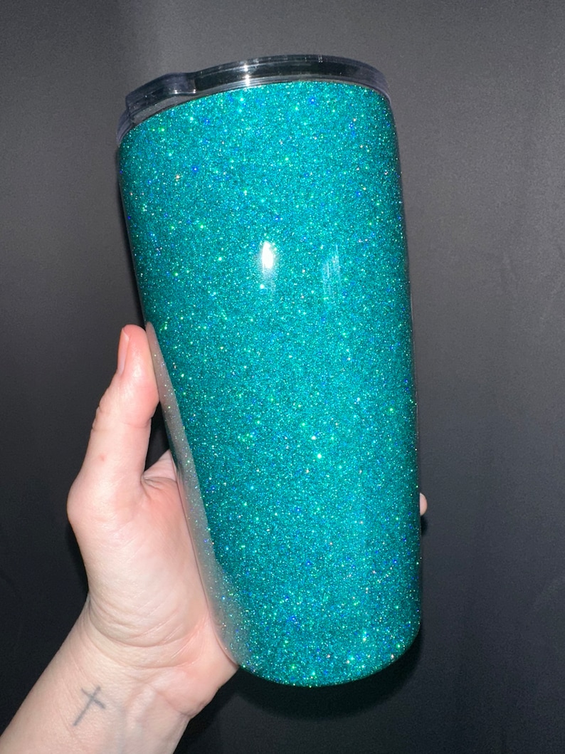 May include: A teal glitter tumbler with a clear lid. The tumbler is made of stainless steel and has a double-wall construction to keep drinks cold or hot for hours.