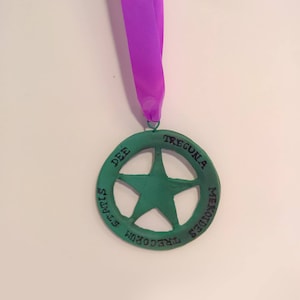 May include: A green medal with a five-pointed star in the center. The medal has the words "TREGUNLA", "DEE", "MEKOUDES", and "TRECORUM" around the edge.