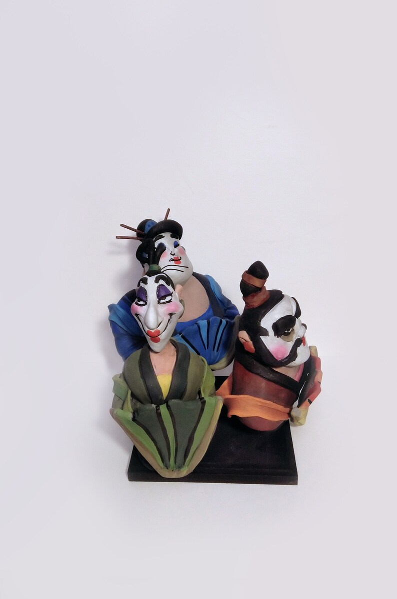 May include: Three hand-painted ceramic figurines of people wearing traditional Japanese clothing. The figurines are painted in black, white, blue, green, yellow, orange, and red. The figurines are standing on a black base.