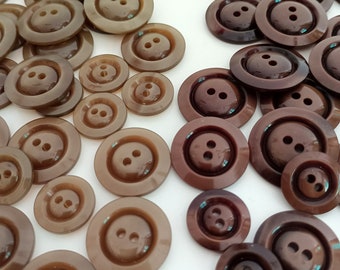 Könnte beinhalten: Sortiment aus braunen und dunkelbraunen Plastikknöpfen mit zwei Löchern. Die Knöpfe sind in verschiedenen Größen und haben ein erhabenes, strukturiertes Design.