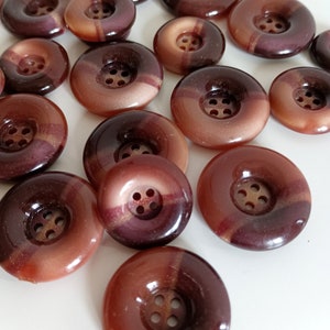 May include: A collection of brown and purple buttons with a shiny finish. The buttons have a raised centre with four holes.