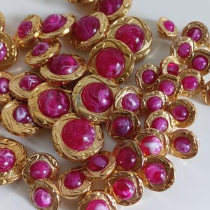 Op de afbeelding: Een verzameling roze en gouden knopen met een swirl-ontwerp. De knopen zijn rond en hebben een verhoogd midden. Ze zijn perfect om een ​​vintage touch toe te voegen aan elk project.