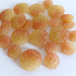 Może przedstawiać: Kolekcja okrągłych, przezroczystych, bursztynowych cukierków. Cukierki są ułożone w losowym wzorze na białym tle.