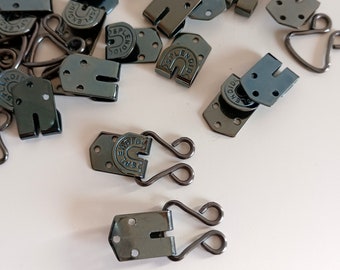 May include: A close-up of a group of black metal hook and eye closures. The hooks are shaped like a 'U' and have a small metal loop on each side. The eyes are flat and have a small hole in the center. The hooks and eyes are all labeled with the word "Splendid".