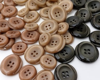 Könnte beinhalten: Eine Sammlung brauner und schwarzer Knöpfe mit vier Löchern. Die Knöpfe sind aus einem glatten, glänzenden Material gefertigt.