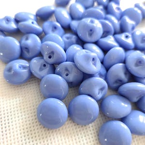 Peut inclure: Un tas de boutons ronds bleu clair avec une finition brillante. Chaque bouton a un petit trou pour la couture. Les boutons sont dispersés sur une surface blanche texturée. Ces boutons sont parfaits pour les projets de couture et d'artisanat.
