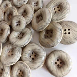 May include: A collection of 12 beige and gray buttons with a woodgrain pattern and four holes each. The buttons are arranged in a random pattern on a white surface.