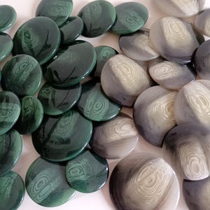 Op de afbeelding: Een verzameling ronde, groene en grijze knopen met een draaiend patroon. De knopen zijn gemaakt van een glad, glanzend materiaal.