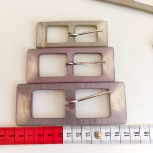 the buckles are photographed next to a tape measure
Three available size