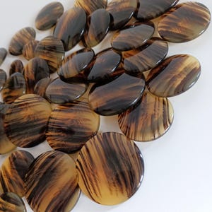 Puede incluir: Un conjunto de botones ovalados y redondos con un diseño de carey. Los botones varían en tamaño y forma, con una mezcla de tonos marrón oscuro y ámbar. El acabado brillante realza las estrías naturales.
