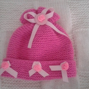 May include: Pink knitted hat with a white ribbon and pink flower embellishments.