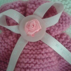 May include: A pink knitted baby hat with a white satin ribbon and a pink fabric flower.