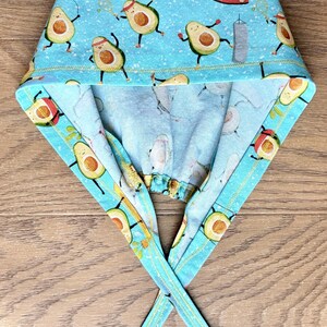 May include: A light blue scrub cap with a repeating pattern of cartoon avocados in various yoga poses and activities. The cap has a light blue background and a yellow trim. The ties are also light blue with a yellow trim.