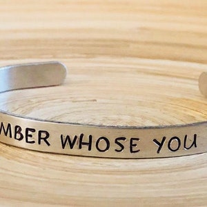 May include: A silver metal bracelet with the inscription "Remember Whose You Are".