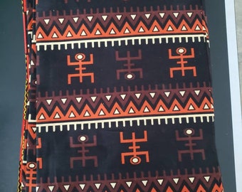 May include: A stack of fabric with a black background and a repeating pattern of orange, brown, and white geometric shapes. The pattern includes stylized human figures and zigzags.