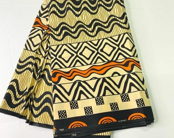 May include: A folded fabric with a geometric pattern in black, orange, and white on a beige background. The fabric has a repeating pattern of waves, diamonds, and zigzags. The fabric is labeled with the text "TEX" and "415747".