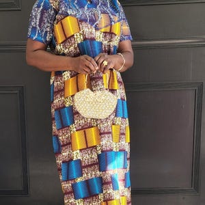 May include: A woman wearing a blue, yellow, and brown patterned dress with a matching head wrap. She is holding a gold beaded clutch purse.
