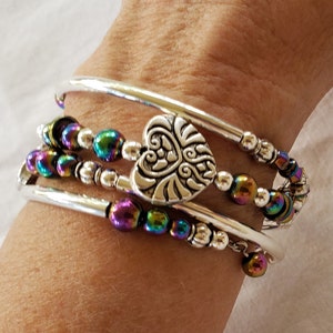 May include: A silver bracelet with a heart charm and iridescent beads. The bracelet is made of three silver bands and a strand of iridescent beads.