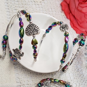 May include: Three silver bangle bracelets with iridescent rainbow coloured beads. The bracelets feature a silver heart charm, a silver turtle charm, and a silver flower charm.
