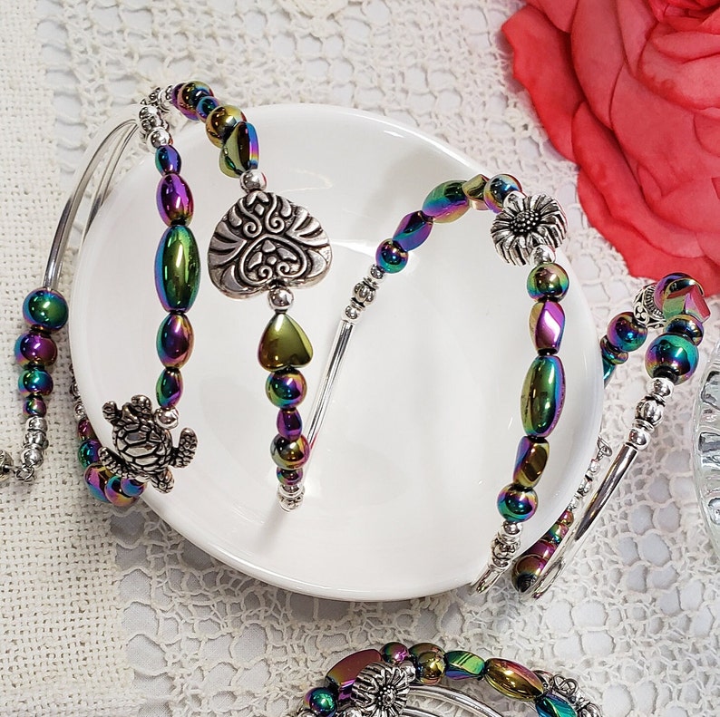 May include: Three silver bangle bracelets with iridescent rainbow coloured beads. The bracelets feature a silver heart charm, a silver turtle charm, and a silver flower charm.