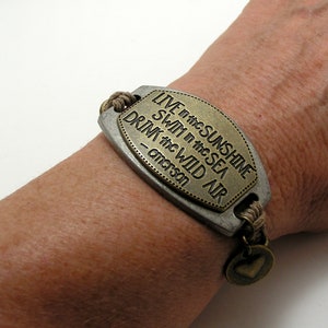 Peut inclure: Un bracelet en cuir marron avec un charme en m&eacute;tal qui dit "LIVE in the SUNSHINE SWIM in the SEA DRINK the WILD AIR -  anderson".