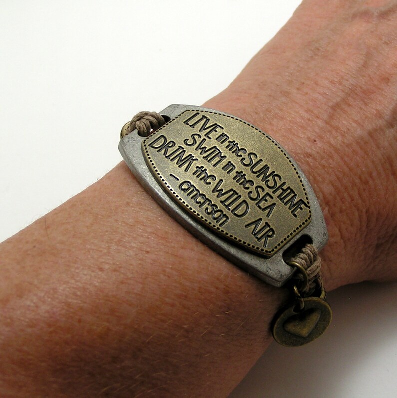 Peut inclure: Un bracelet en cuir marron avec un charme en m&eacute;tal qui dit "LIVE in the SUNSHINE SWIM in the SEA DRINK the WILD AIR -  anderson".