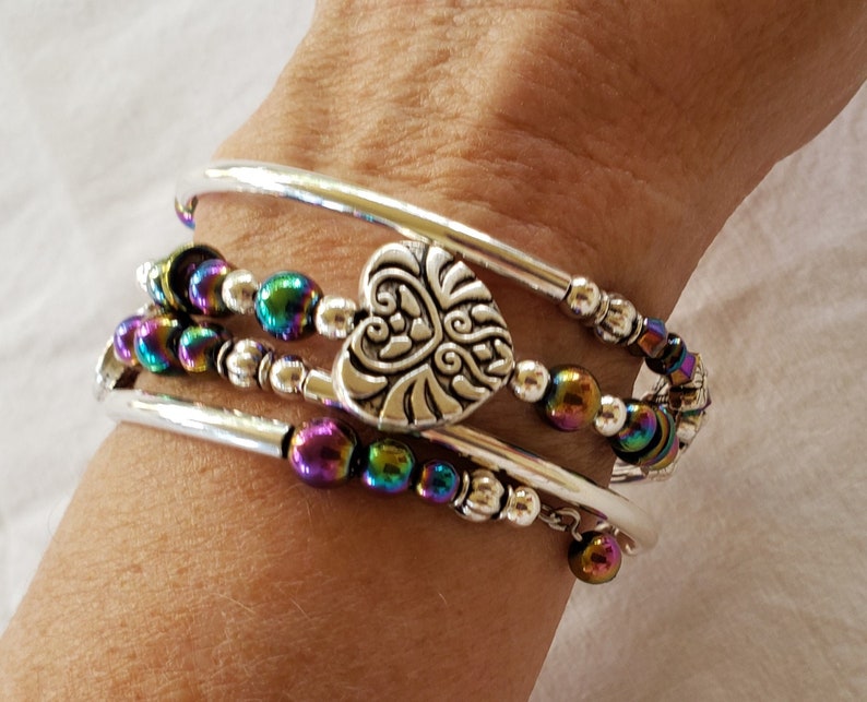 May include: A silver bracelet with a heart charm and iridescent beads. The bracelet is made of three silver bands and a strand of iridescent beads.