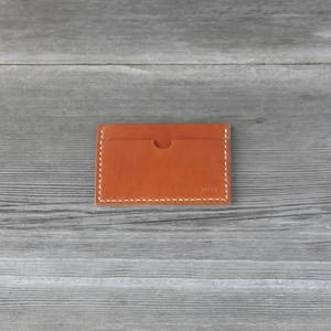 May include: A brown leather card holder with white stitching. The card holder is on a gray wooden surface.