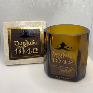 May include: A brown glass bottle of Don Julio 1942 tequila. The bottle has a gold label with the brand name and year. The bottle is sitting on a white surface.