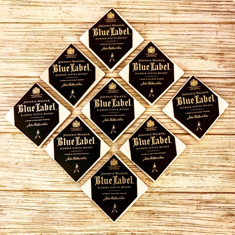 May include: Eight square coasters with a white background and black diamond-shaped design. The diamond features the Johnnie Walker Blue Label logo with gold lettering. The text reads "JOHNNIE WALKER, Blue Label, BLENDED SCOTCH WHISKY".