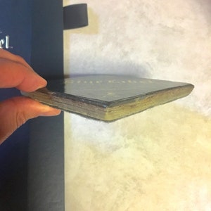 May include: Close-up of the spine of a hardback book with a black cover and gold lettering. The book is slightly worn and has a few scratches.