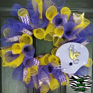 Puede incluir: Una corona de malla morada y amarilla con un casco de f&uacute;tbol gris que presenta una mascota negra y amarilla. La corona est&aacute; decorada con una cinta de chevron morada y blanca y un coraz&oacute;n de estampado de cebra con el texto "gurl gone craft".