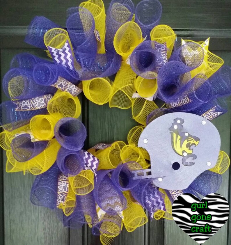 Puede incluir: Una corona de malla morada y amarilla con un casco de f&uacute;tbol gris que presenta una mascota negra y amarilla. La corona est&aacute; decorada con una cinta de chevron morada y blanca y un coraz&oacute;n de estampado de cebra con el texto "gurl gone craft".