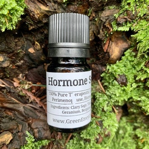 May include: A small, dark brown glass bottle with a black cap. The label reads "Hormone Support 100% Pure Therapeutic Grade Perimeno use, Hormone Balancing Blend Ingredients: Clary Sage, Ylang Ylang, Geranium, Bergamot www.GreenEnvyCo.com"