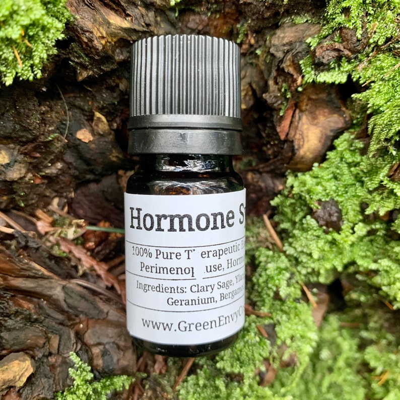 May include: A small, dark brown glass bottle with a black cap. The label reads "Hormone Support 100% Pure Therapeutic Grade Perimeno use, Hormone Balancing Blend Ingredients: Clary Sage, Ylang Ylang, Geranium, Bergamot www.GreenEnvyCo.com"