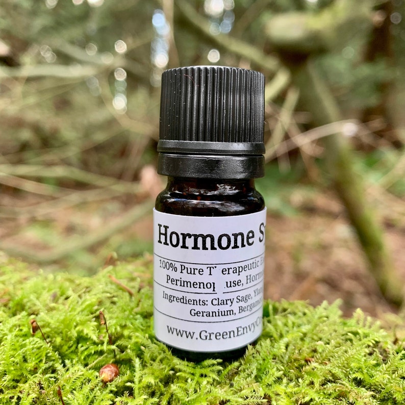 Very small brown bottle with a white label and a black dropper top, on top of some moss with forest in the background.