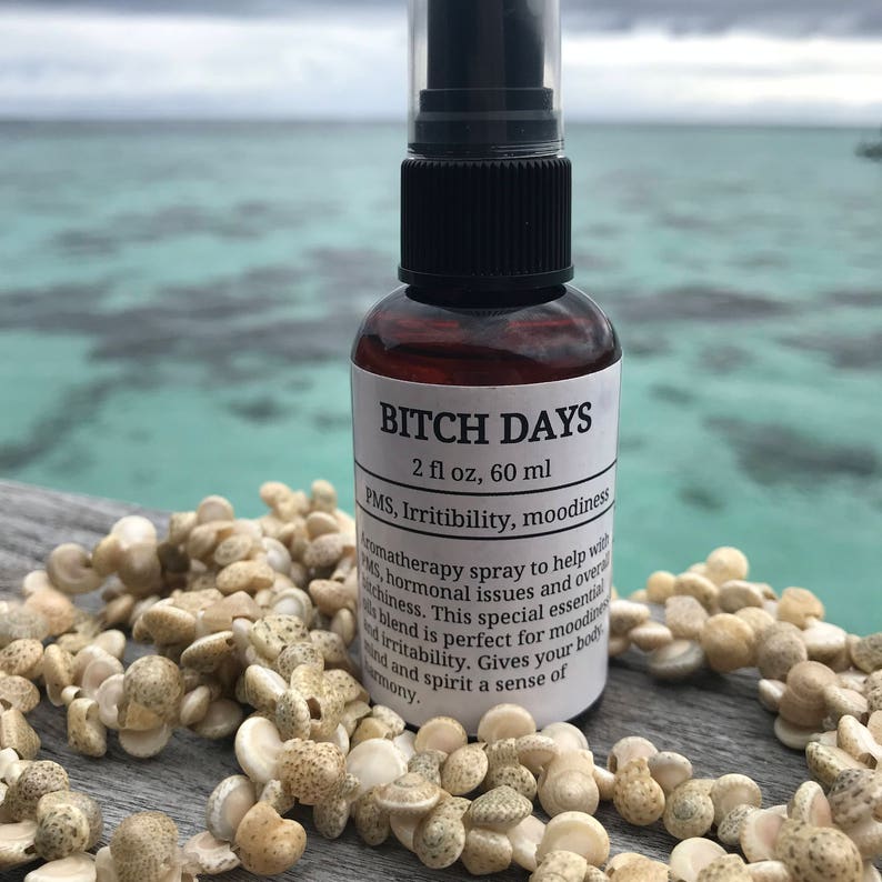 May include: A brown glass bottle with a black spray top and a white label that reads "BITCH DAYS 2 fl oz, 60 ml PMS, Irritibility, moodiness aromatherapy spray to help with PMS, hormonal issues and overall moodiness. This special essential blend is perfect for moodiness and irritability. Gives your body and spirit a sense of harmony."