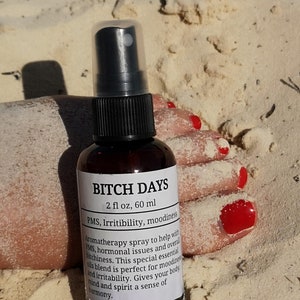 May include: A brown glass bottle with a black spray top and a white label that reads "BITCH DAYS 2 fl oz, 60 ml PMS, Irritibility, moodiness Aromatherapy spray to help with PMS, hormonal issues and overall bitchiness. This special essential oils blend is perfect for moodiness and irritability. Gives your body, mind and spirit a sense of harmony."