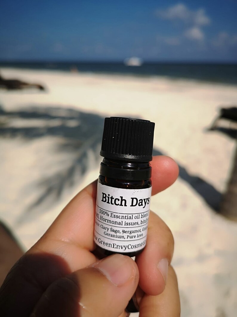 May include: A small glass bottle with a black cap and a white label that reads "Bitch Days 100% Essential oil blend for Hormonal issues, bitch Clary Sage, Bergamot, Grapefruit Geranium, Pure love www.GreenEnvyCosmetics.com".