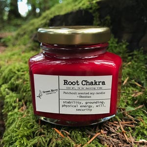 Small clear glass container with a bright red candle inside and a gold lid, placed on some moss with forest in the background.