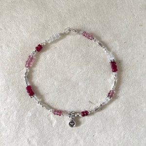 May include: A silver bracelet with pink and white beads and a small heart charm.
