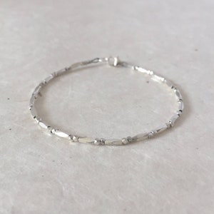 May include: A silver bracelet made of small, faceted, rectangular beads.